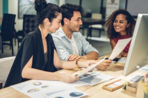 Marketing Executive brainstorming at desk with two colleagues infront of a computer monitor